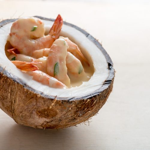 Unos jugosos camarones con salsa de encocado servidos sobre medio coco maduro