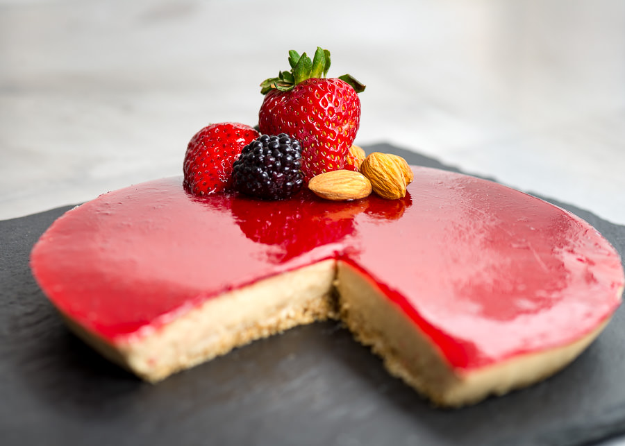 Un cheesecake de ricotta y frutos rojos, decorado por una fresa partida en la mitad, una mora y tres almendras.